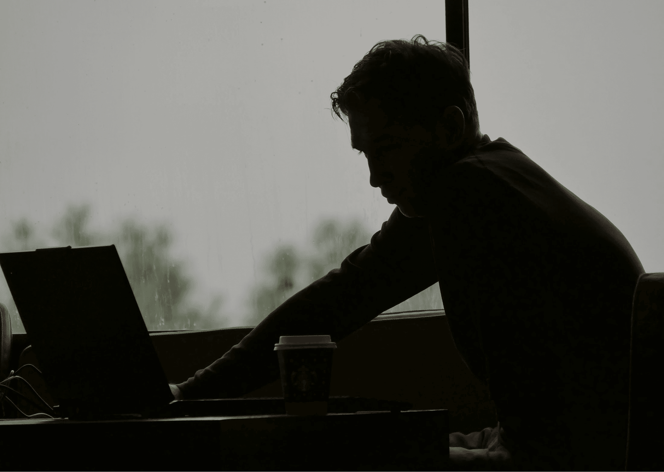 Silhouette of a person by a window focused, working on a laptop